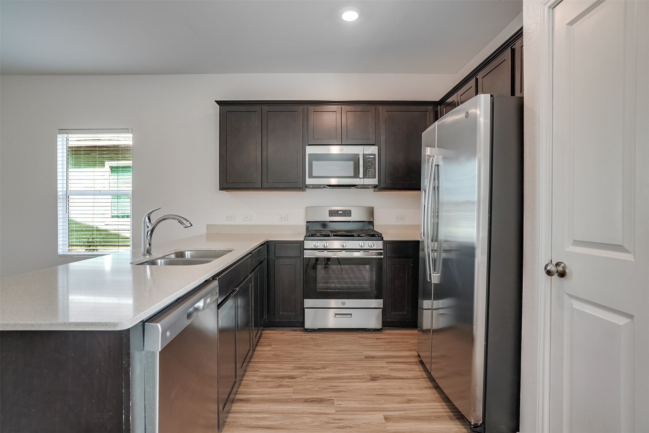 428 Gabbro Gardens Maxwell, TX 78656 - Photo 5 of 26 Kitchen featuring stainless steel appliances, dark wood finish cabinets, light wood-style floors, a peninsula, and recessed lighting
