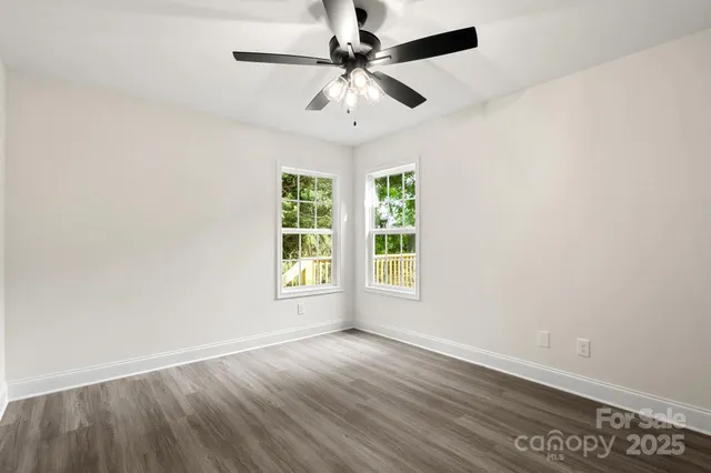 an empty room with wooden floor chandelier fan and windows
