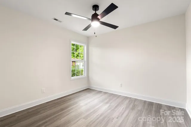 an empty room with wooden floor ceiling fan and windows