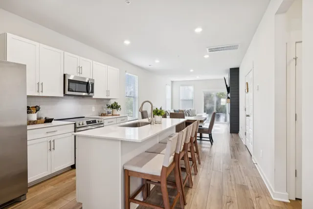 a kitchen with stainless steel appliances granite countertop a stove a sink a microwave a refrigerator a stove and white cabinets with wooden floor