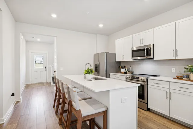 a kitchen with stainless steel appliances a stove a sink a microwave a refrigerator white cabinets and wooden floor