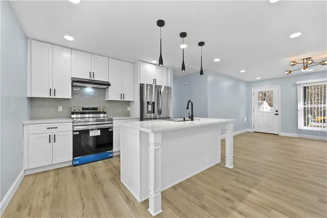 a kitchen with stainless steel appliances kitchen island wooden floors cabinets and a window