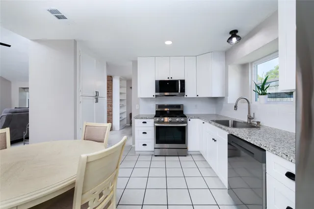 a kitchen with stainless steel appliances a dining table chairs refrigerator and sink