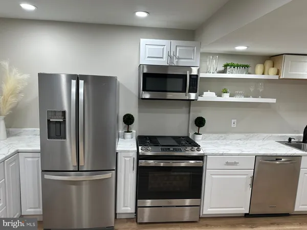a kitchen with stainless steel appliances a refrigerator a stove a sink and white cabinets