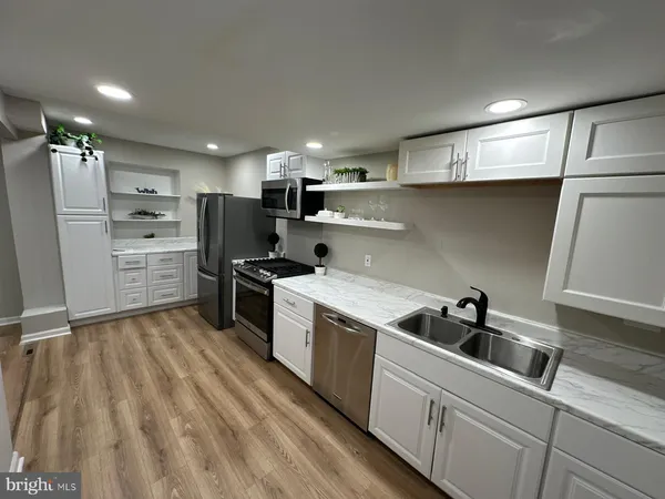 a kitchen with stainless steel appliances white cabinets a sink a stove a microwave and wooden floors