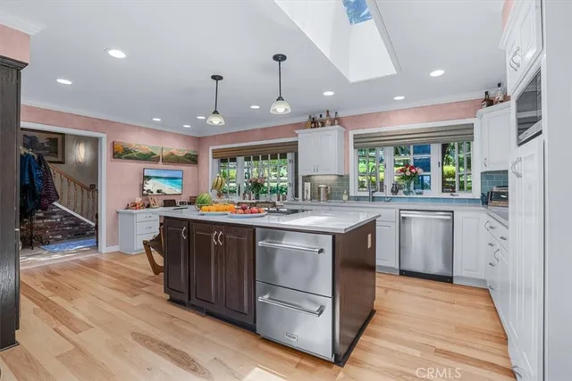 a kitchen with stainless steel appliances kitchen island granite countertop a refrigerator a stove a sink a dining table and chairs with wooden floor