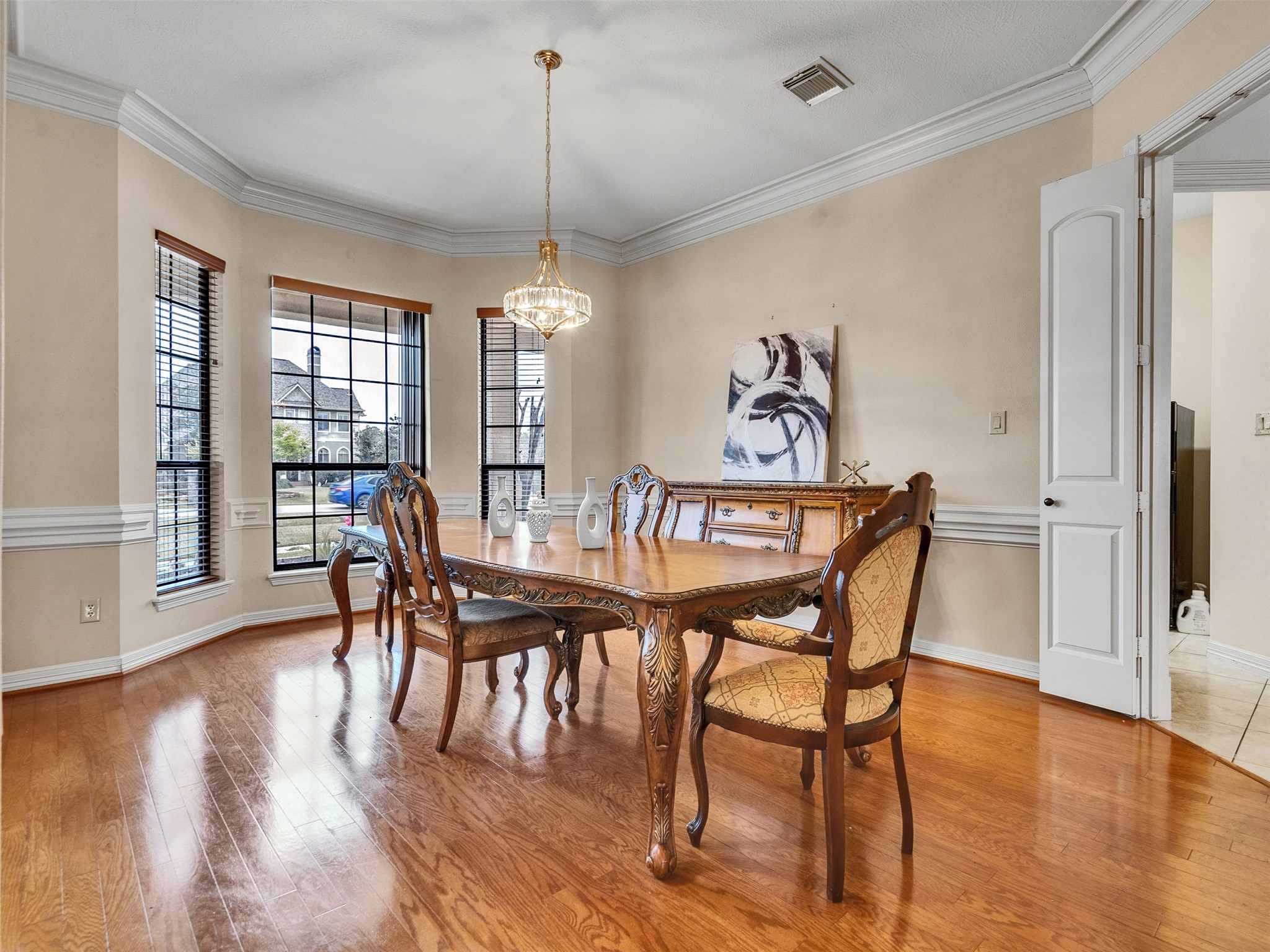 6914 Sandwedge Point Court Spring, TX 77389 - Photo 13 of 50 This elegant dining room features hardwood floors, a large window with ample natural light, a classic wooden dining set, and a stylish chandelier. The space is complemented by crown molding and neutral walls, creating a warm and inviting atmosphere.