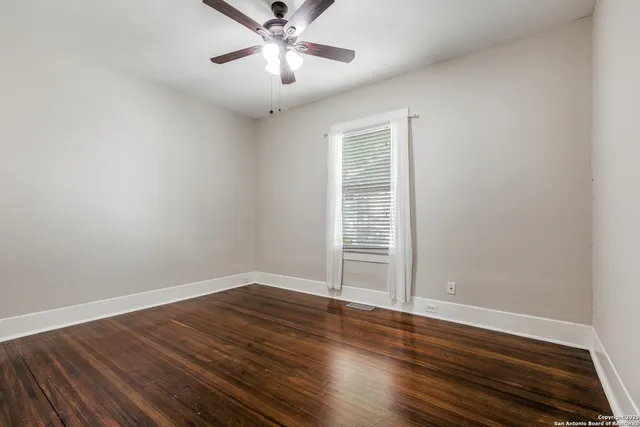 an empty room with wooden floor chandelier fan and windows