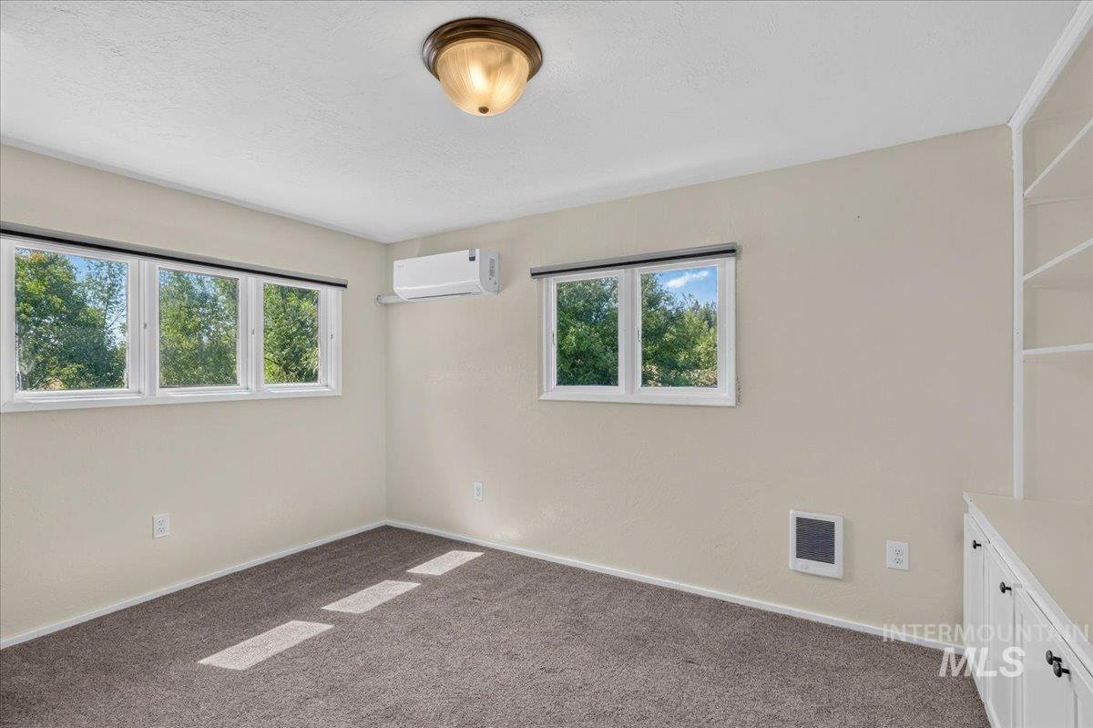 1071 Reynolds Road Princeton, ID 83857 - Photo 37 of 43 Bright room with multiple windows, a ceiling-mounted light fixture, carpeted flooring, a wall-mounted heating unit, and built-in shelving with lower cabinetry