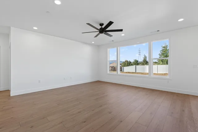 an empty room with wooden floor ceiling fan and windows