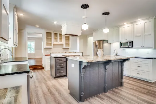 a large kitchen with stainless steel appliances kitchen island granite countertop a stove a sink dishwasher a microwave oven and a dining table with wooden floor