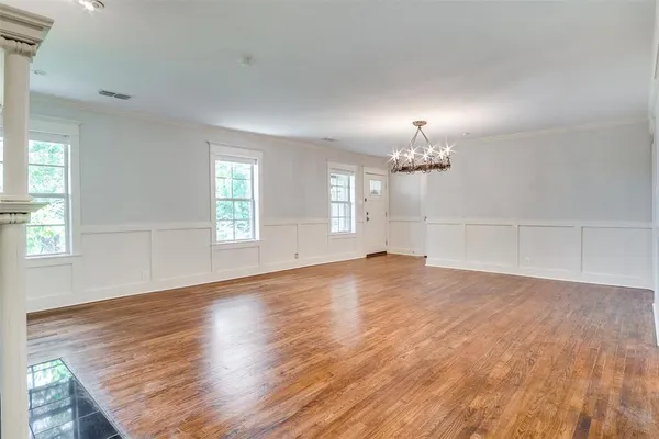 an empty room with wooden floor chandelier and windows
