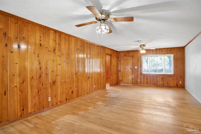 a view of an empty room with wooden floor and fan