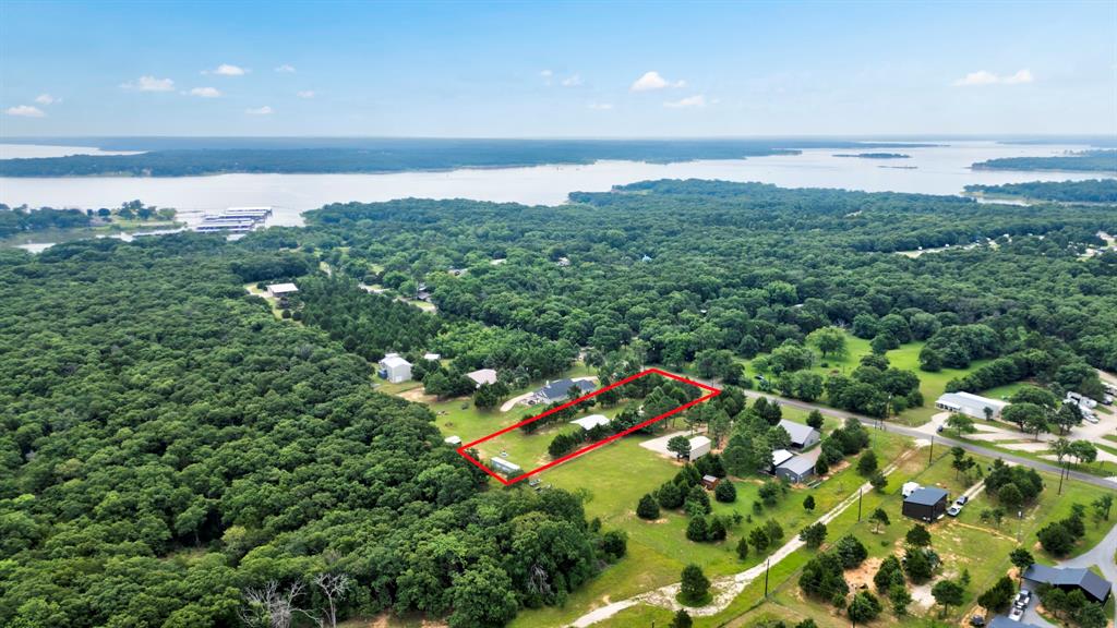 1469 Cedar Mills Road Gordonville, TX 76245 - Photo 9 of 12 Aerial property view featuring a prominent red-outlined parcel, extensive green landscaping, a distant body of water, scattered residential structures, and a clear sky with sparse clouds