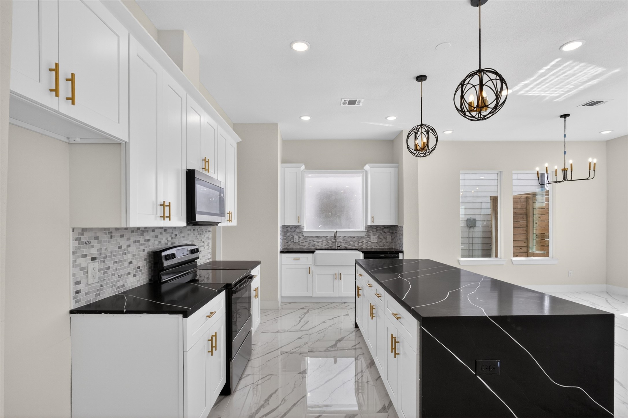 5906 St Augustine Street, Unit F Houston, TX 77021 - Photo 1 of 34 Bright kitchen with a large waterfall-style island, white cabinetry, black countertops, pendant lighting, and open sightlines.