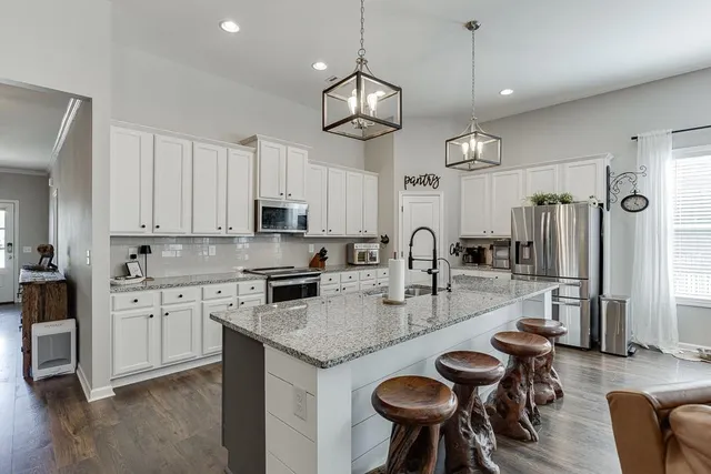 a kitchen with stainless steel appliances granite countertop a stove top oven a sink a dining table and chairs with white cabinets