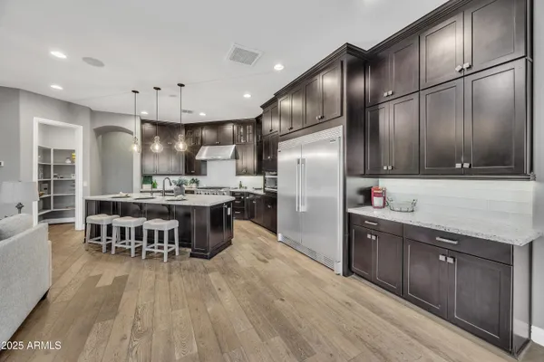 a kitchen with stainless steel appliances kitchen island granite countertop a refrigerator a stove a sink a dining table and chairs with wooden floor