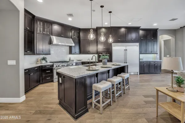 a kitchen with stainless steel appliances kitchen island granite countertop a stove a refrigerator a sink a dining table and chairs with wooden floor