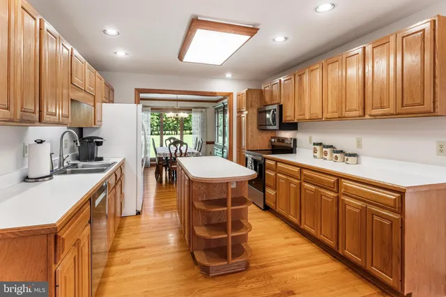 a kitchen with stainless steel appliances granite countertop wooden cabinets a sink dishwasher a stove and a refrigerator with wooden floor