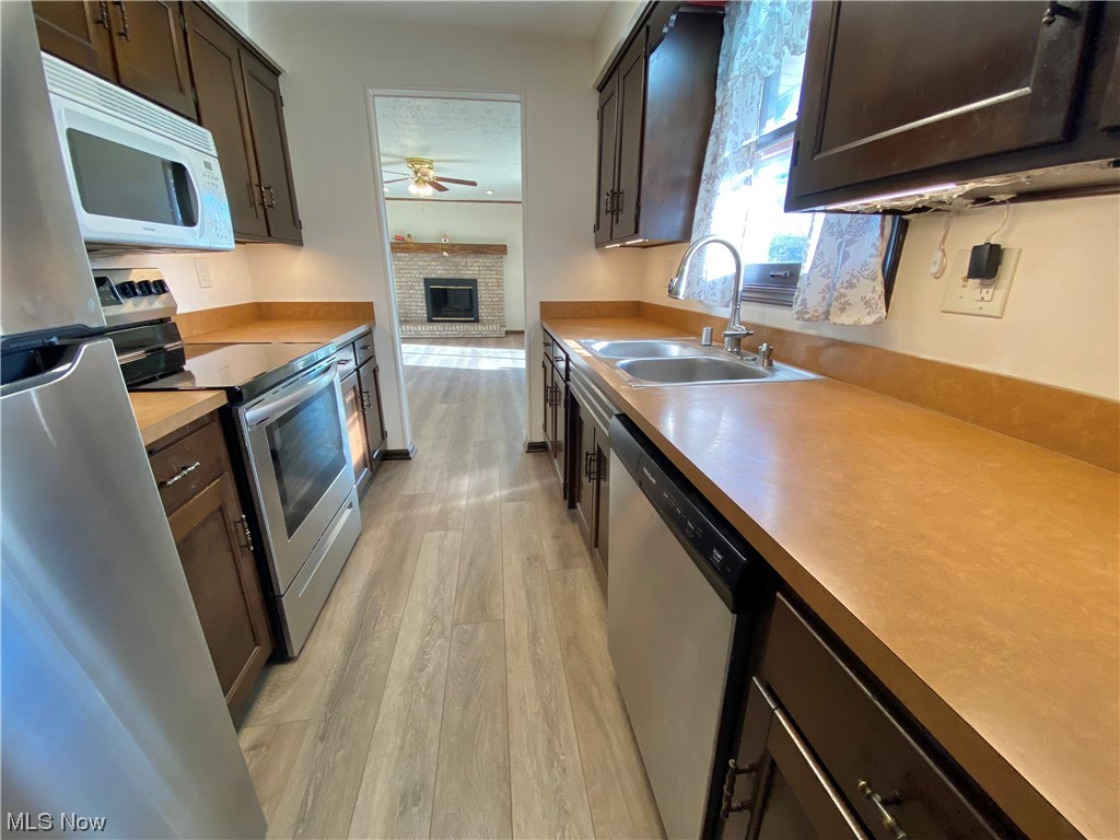 23551 Sandy Creek Road Minerva, OH 44657 - Photo 6 of 35 Kitchen featuring sink, light hardwood / wood-style flooring, a brick fireplace, stainless steel appliances, and ceiling fan