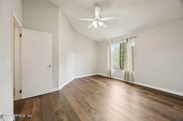 an empty room with wooden floor fan and windows