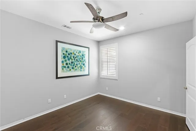 an empty room with wooden floor ceiling fan and windows