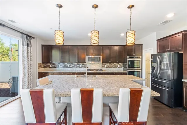 a kitchen with stainless steel appliances granite countertop a sink a stove a refrigerator a kitchen island a cabinetry and a chandelier