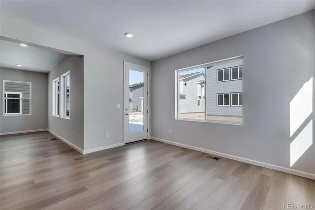 a view of an empty room with wooden floor and a kitchen