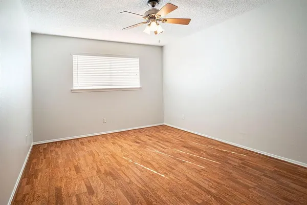 an empty room with wooden floor chandelier fan and windows