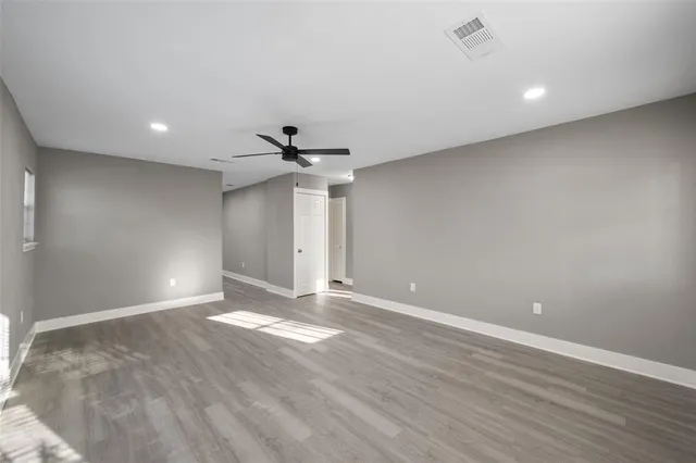 a view of an empty room with wooden floor and a ceiling fan