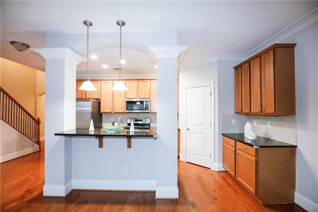 a kitchen with stainless steel appliances granite countertop a refrigerator a sink dishwasher a stove and a dining table with wooden floor