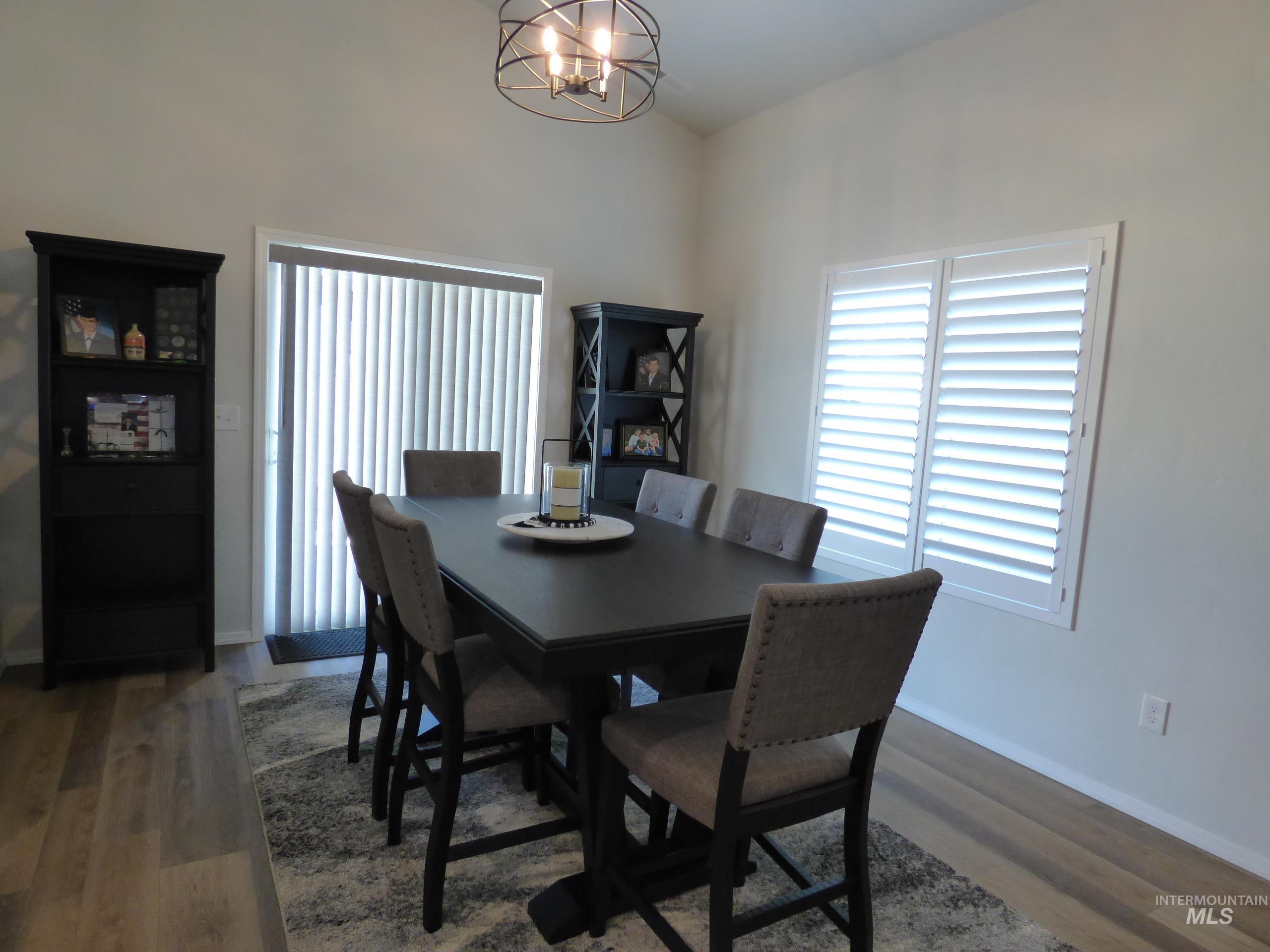 2708 East Buckaroo Drive Kuna, ID 83634 - Photo 10 of 48 Dining area featuring wood-finish flooring, a contemporary chandelier, white window shutters, and a vertical blind-equipped sliding glass door