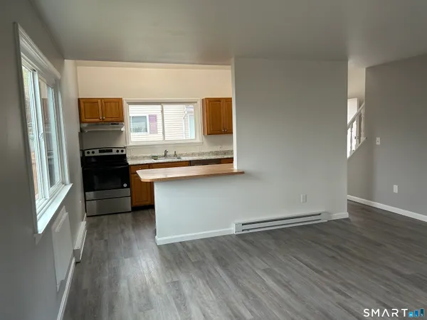 an empty room with wooden floor kitchen view and windows