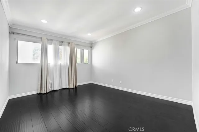 an empty room with wooden floor and windows with curtains