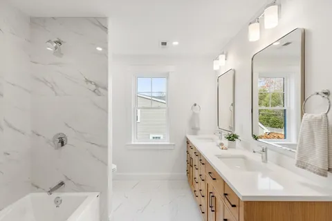 a bathroom with a tub sink double vanity granite and a mirror