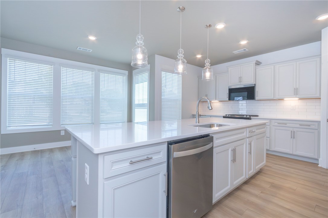 607 WH Kay Lane Anderson, SC 29621 - Photo 11 of 48 A well-lit kitchen boasts pristine white cabinetry, a spacious island with a sink, and integrated stainless steel appliances.
