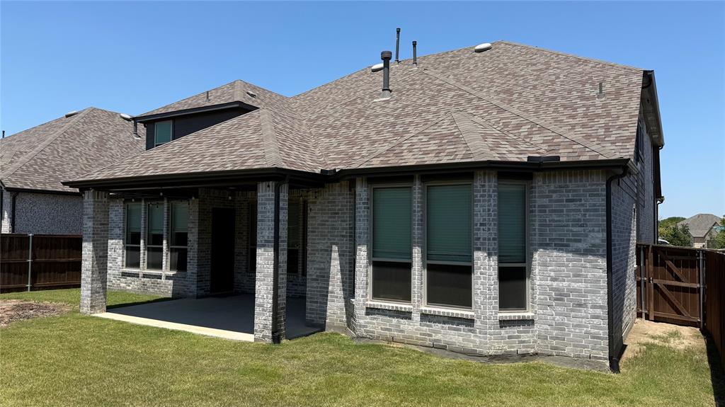 9628 Boulder Pt Road Oak Point, TX 75068 - Photo 25 of 35 Rear exterior featuring a covered patio with string lighting, gray brick construction, dark gutters, and a shingled roof