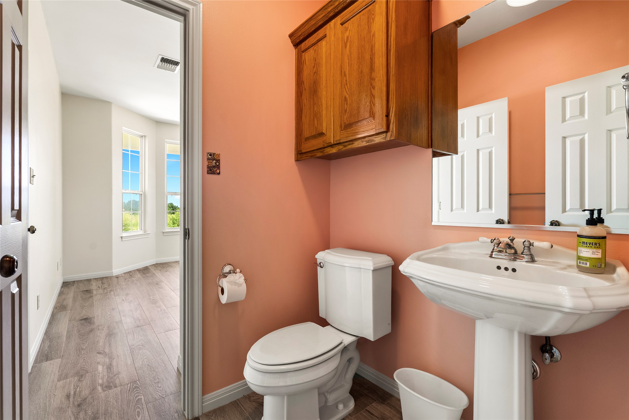 928 Upper Elgin River Road Elgin, TX 78621 - Photo 28 of 40 Pedestal sink with a two-handle faucet, a toilet, and an overhead wood-finish cabinet.