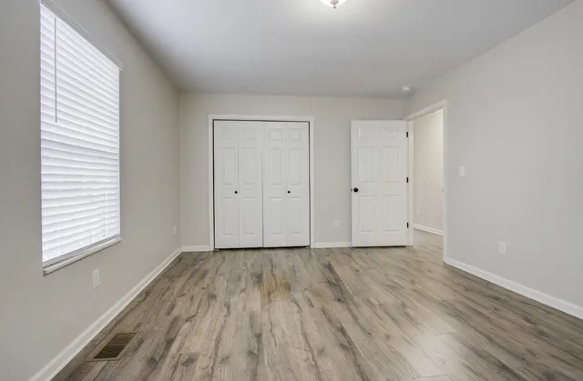 a view of an empty room with wooden floor and a window