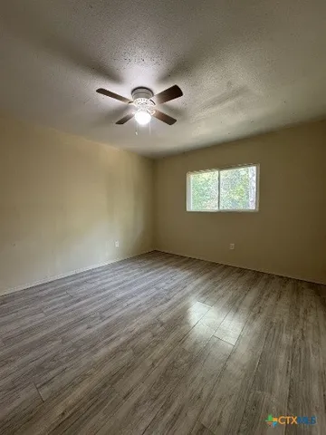 an empty room with wooden floor ceiling fan and windows