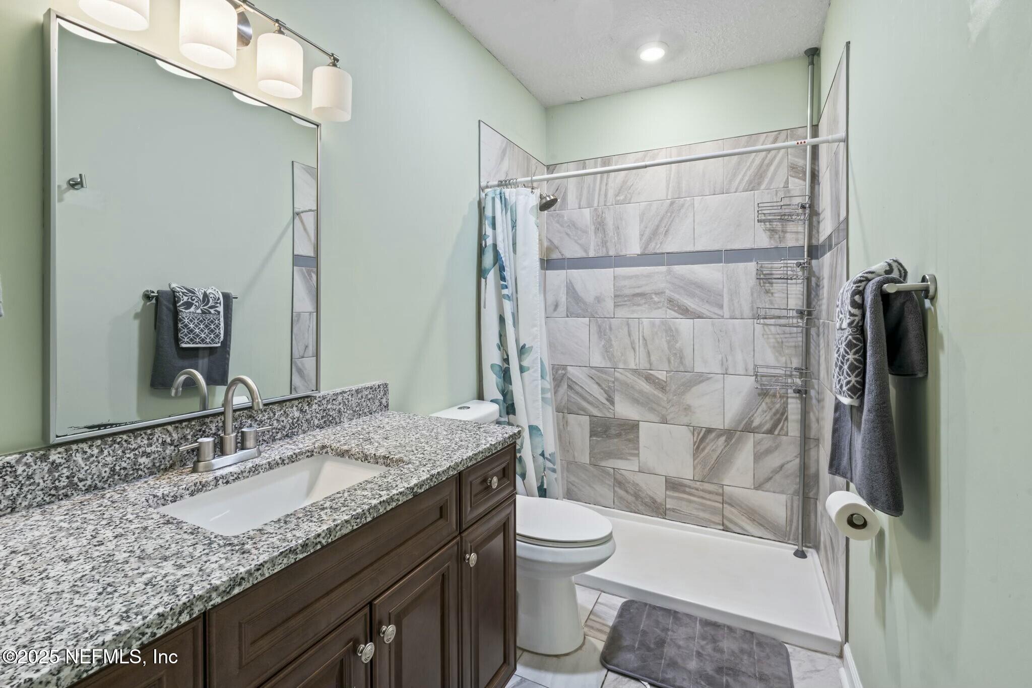 6053 Firestone Road Jacksonville, FL 32244 - Photo 16 of 34 a bathroom with a granite countertop sink toilet and shower