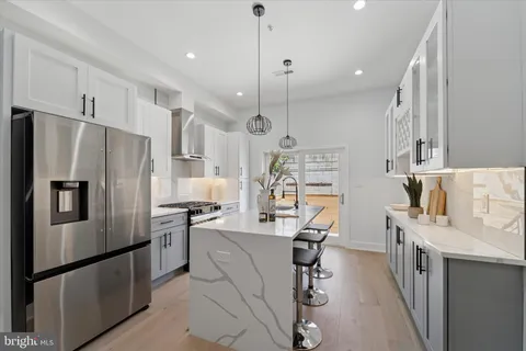 a kitchen with stainless steel appliances kitchen island granite countertop a refrigerator a oven a sink dishwasher and white cabinets with wooden floor
