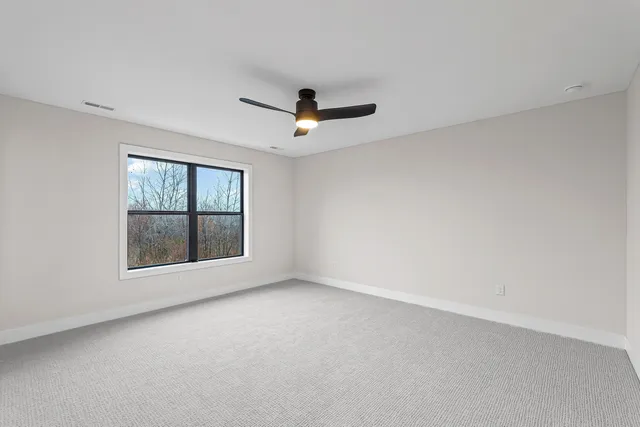 an empty room with ceiling fan and windows