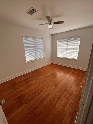 an empty room with wooden floor fan and windows