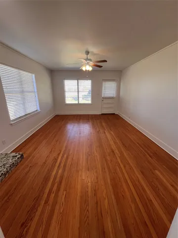 an empty room with wooden floor chandelier fan and windows