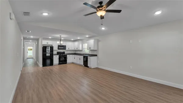 a view of an empty room with kitchen appliances and a ceiling fan