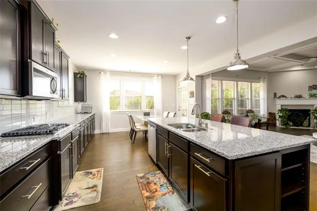 a large kitchen with stainless steel appliances kitchen island a stove a refrigerator a oven a sink a dining table and chairs with wooden floor