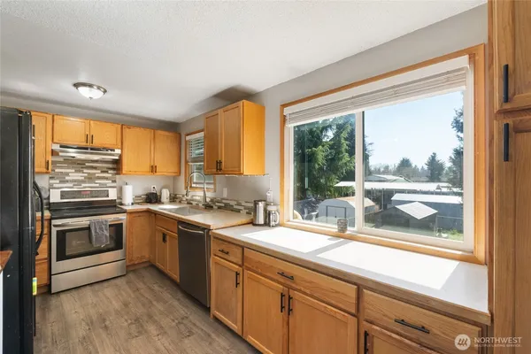 a kitchen with stainless steel appliances kitchen island granite countertop a refrigerator a stove a sink dishwasher a dining table and chairs with wooden floor
