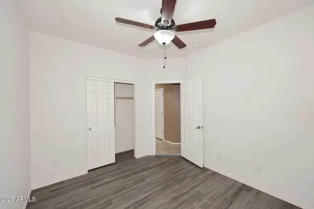 an empty room with wooden floor ceiling fan and windows
