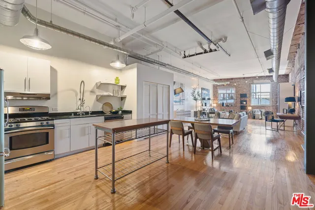 a open kitchen with stainless steel appliances granite countertop a stove top oven a dining table and chairs with wooden floor